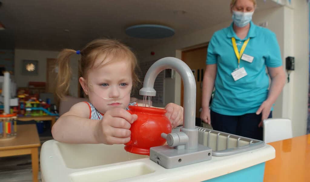 A supported child enjoys filling a teapot from a toy tap. We attempted to explain to her how firms can donate residual client balances to support our hospice but she preferred to do this,