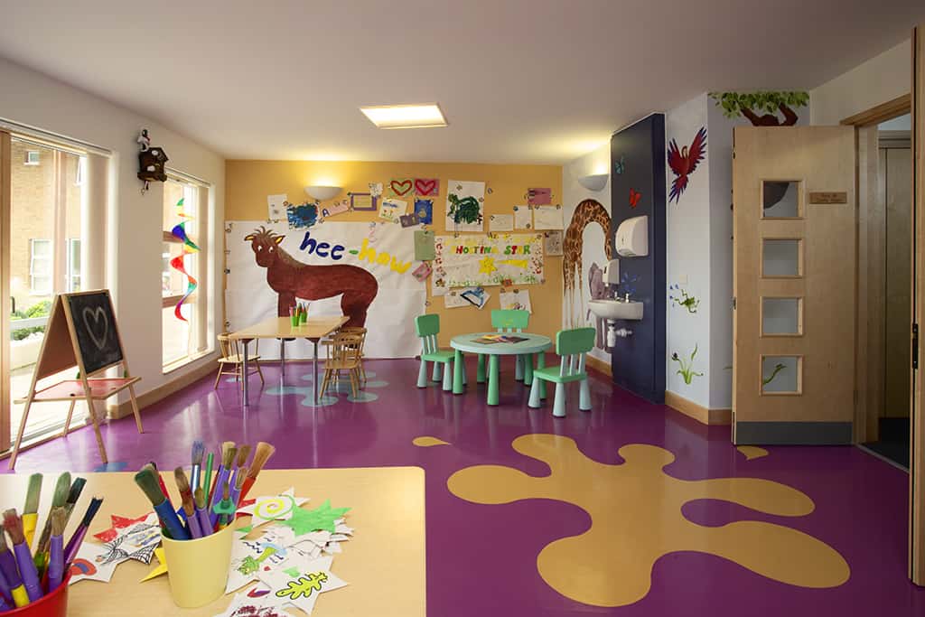 Giant decorative paint splatter on the bright pink floor with tables and chairs full of arts and crafts material.