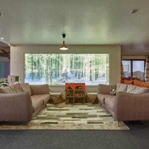 Massive room with a luminous screen on the wall showing a forest, next to multiple sofas and a plethora of toys.