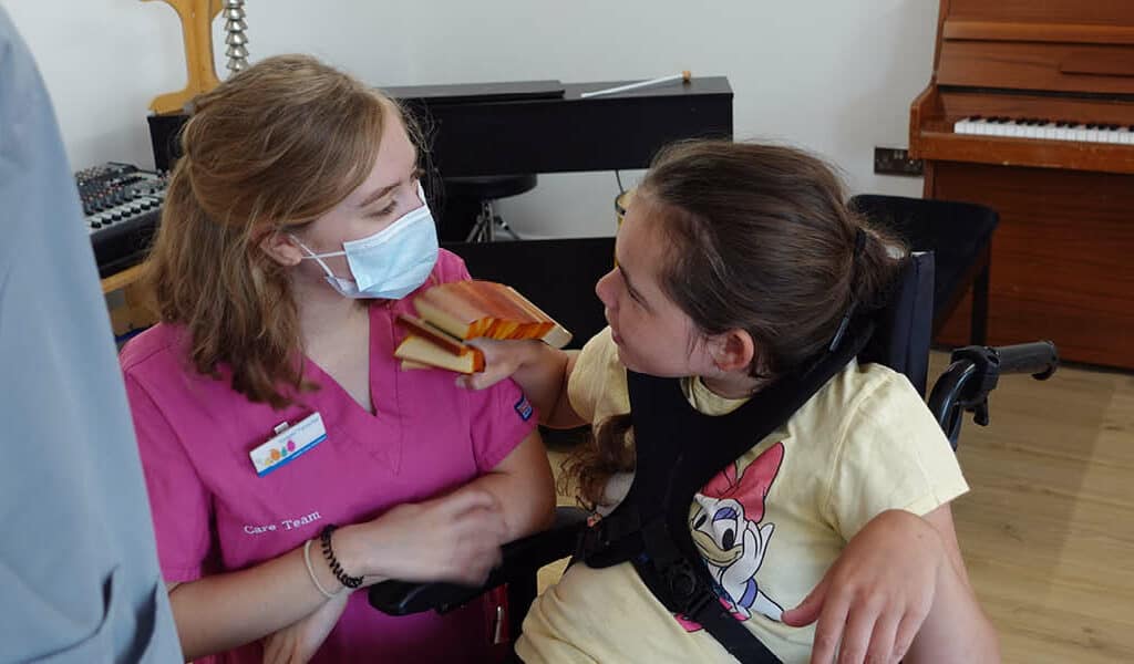 Supported child in wheelchair looks at nurse whilst playing with a shaky musical instrument