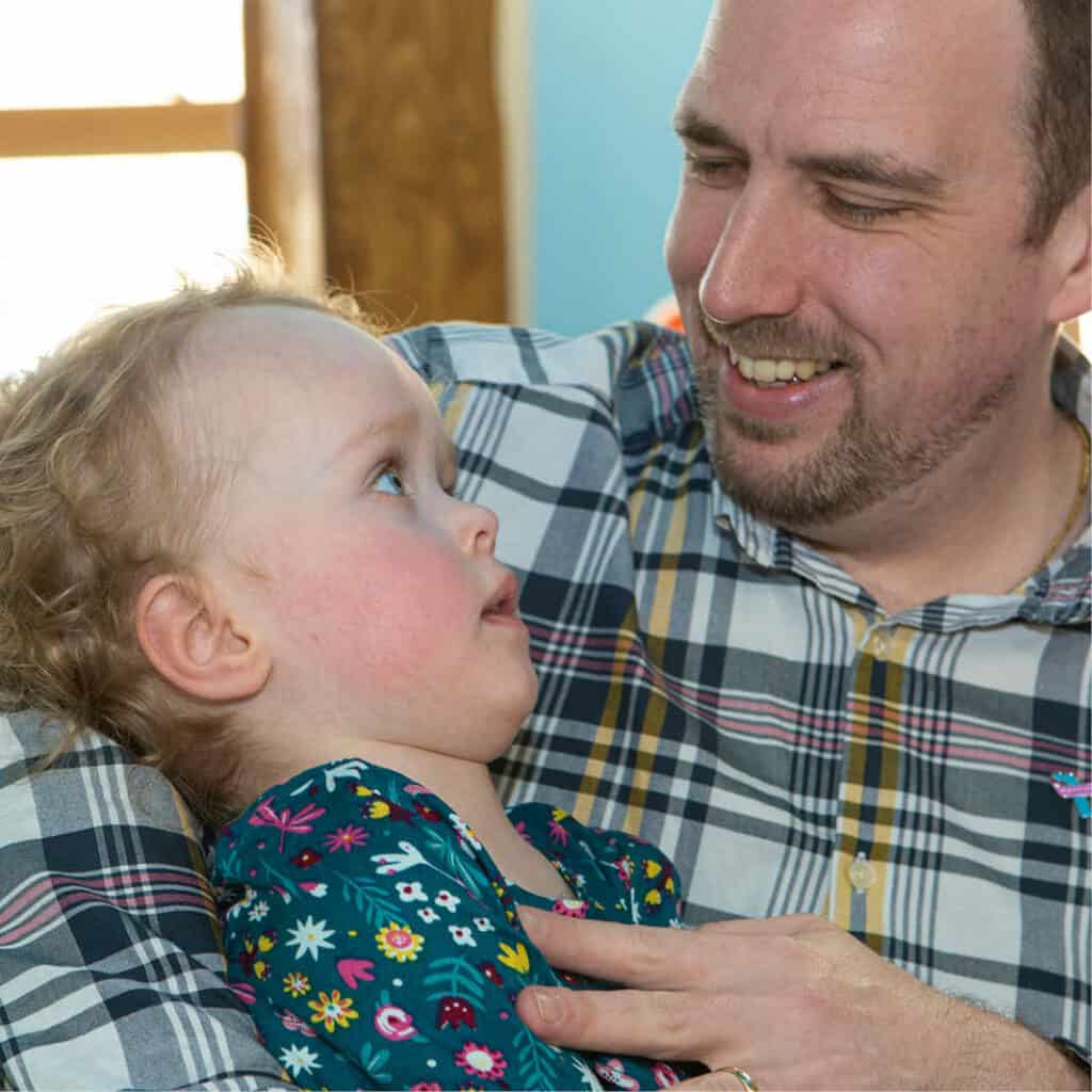 Dad smiles as he cuddles his blonde haired daughter at the hospice