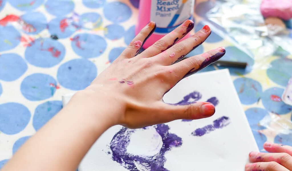Child creating a art picture of their hand print in purple paint