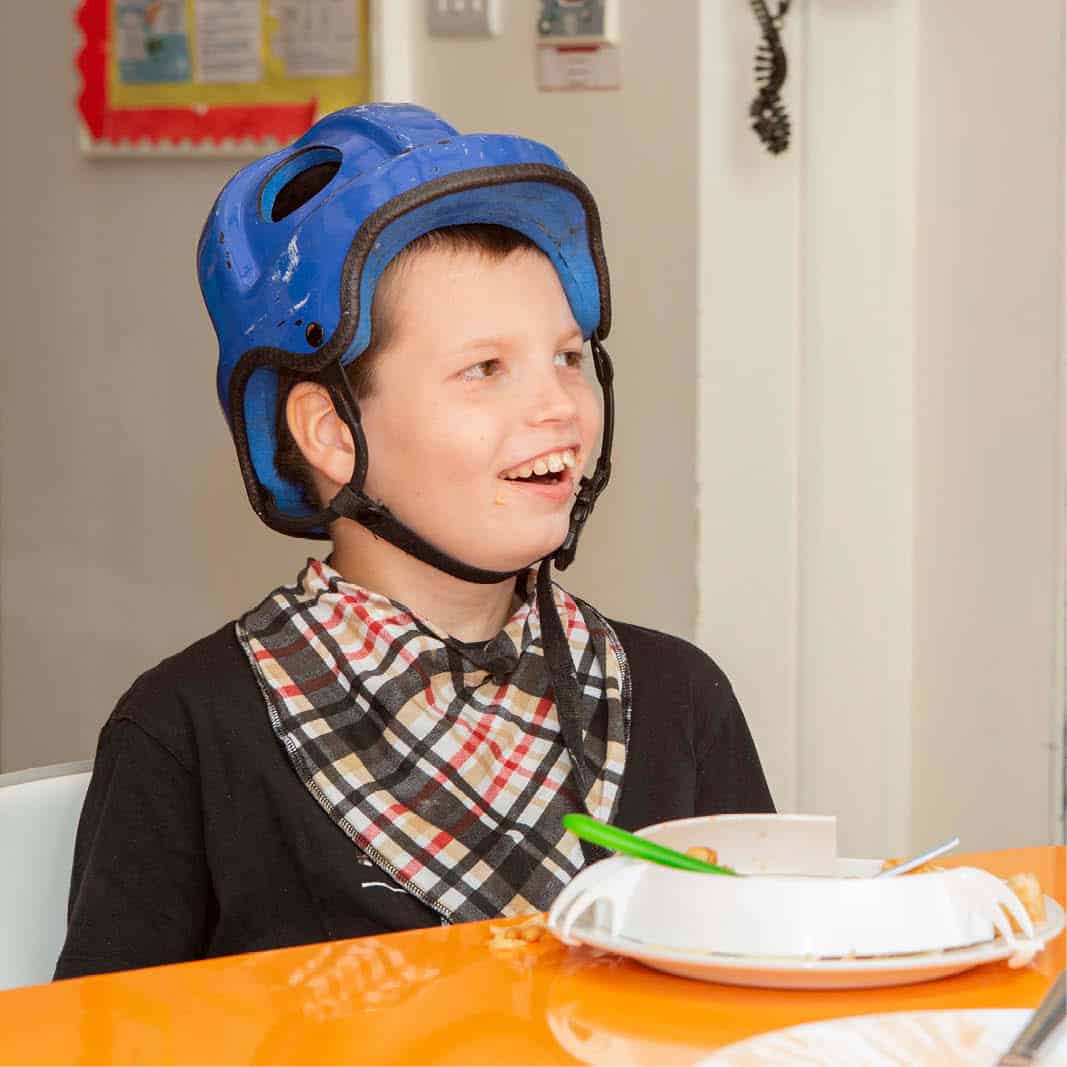 Young boy wearing a protective helmet smiles sitting at a table