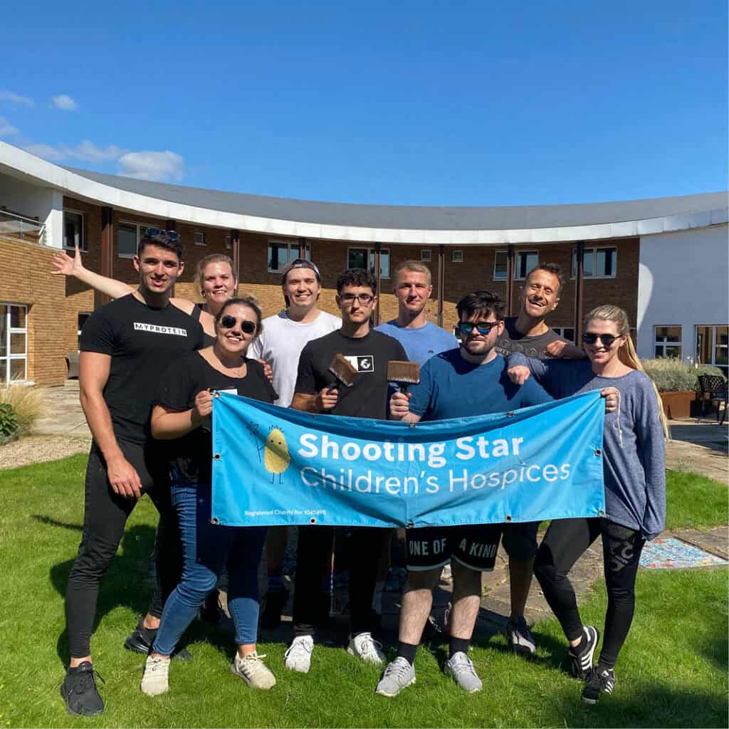 Young group of corporate supporters hold up Shooting Star banner in the garden of the hospice