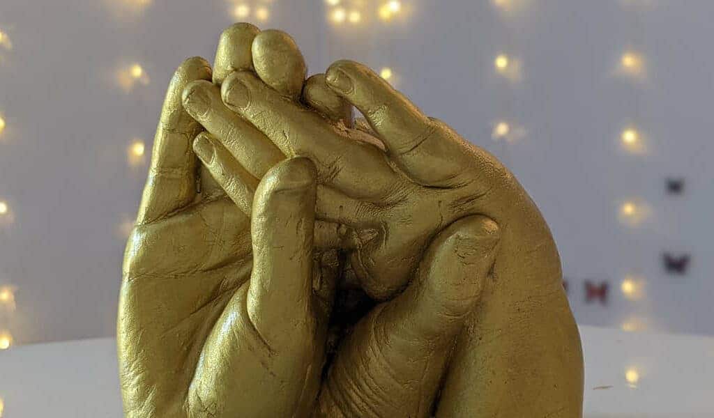 A cast of a child's hand being held by a parent's, decorated with gold paint.