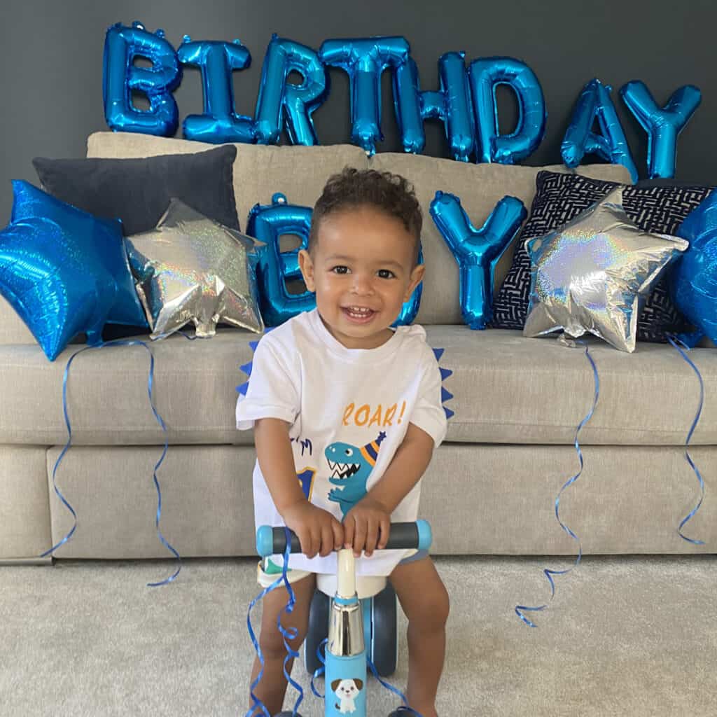 Young boy on scooter in front of balloons that say Birthday Boy