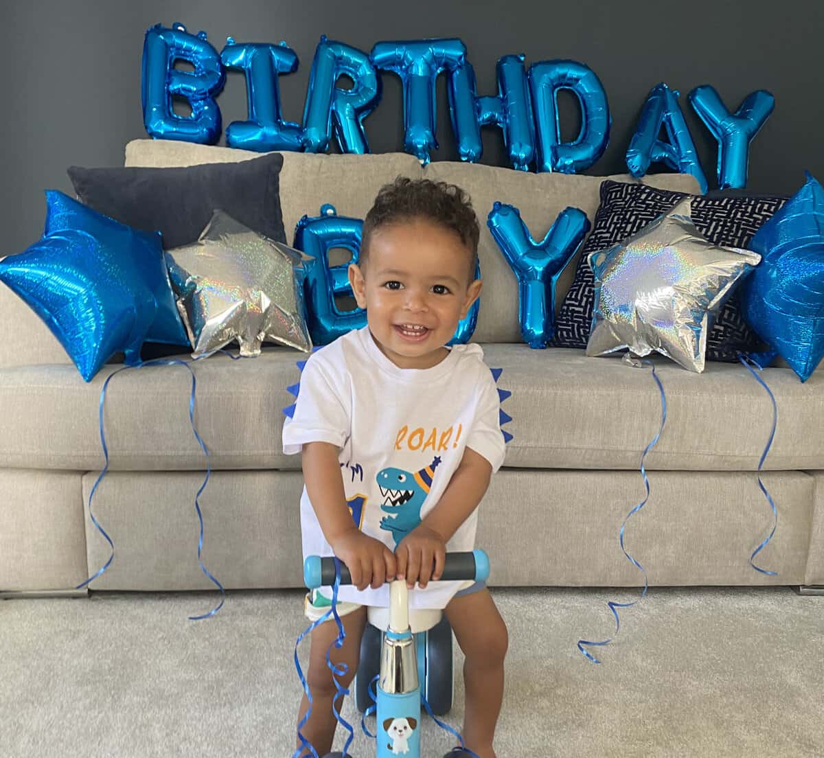 Young boy on scooter in front of balloons that say Birthday Boy