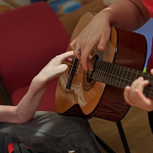 A child's hand touching a guitar being held by a music therapist.