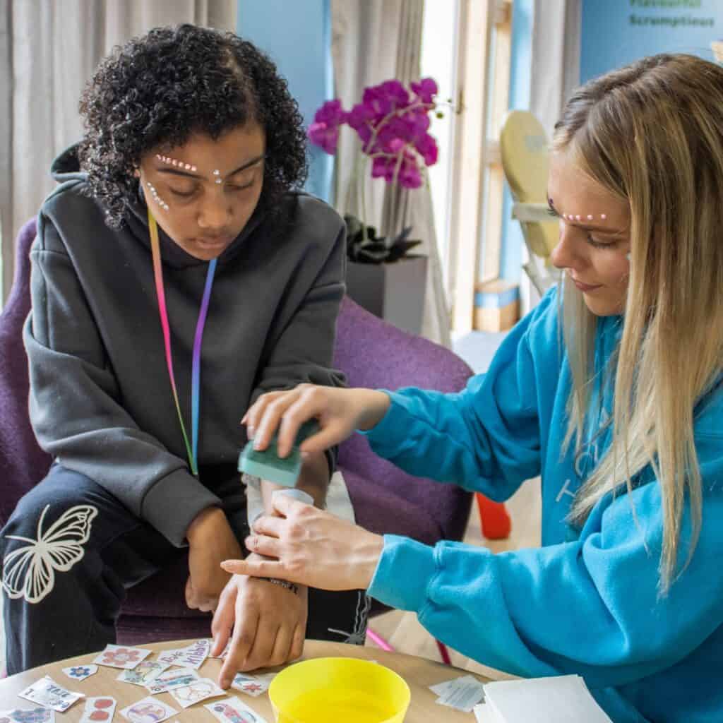 A Shooting Star worker decorating a supported child's hand with glittery stars at a siblings day event.