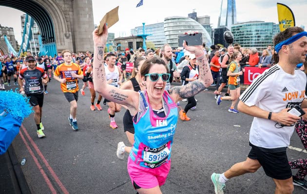 Smiling marathon runner waving her arms as she crosses Tower Bridge