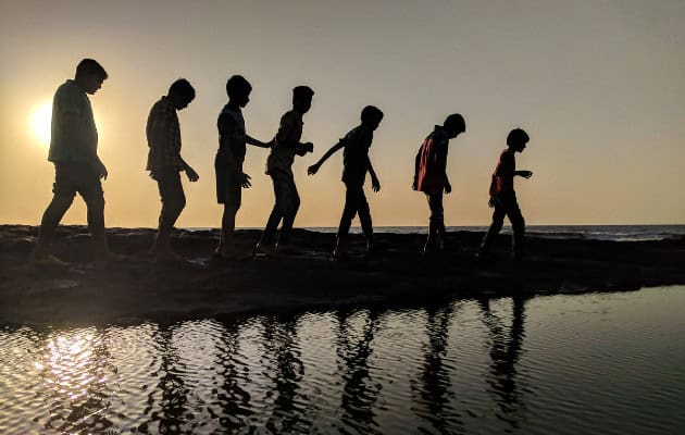 silhouettes of a group of children walking by the sea.
