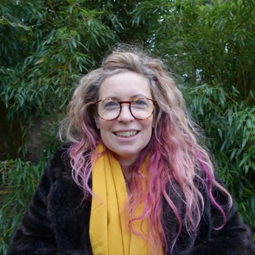 Dr Katherine Hunt, a woman with long blond hair tinted purtple, wearing a scarf.