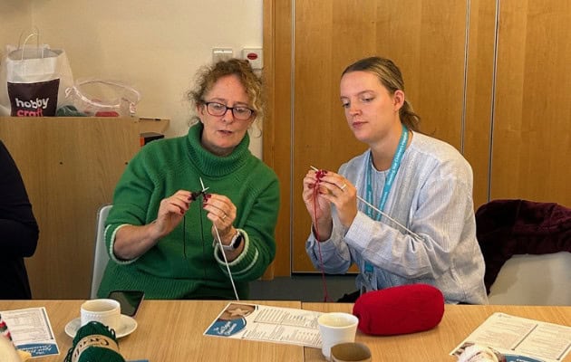 Two people knitting (well one is attempting to knit but they are doing their best)