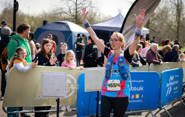 Women wearing a Shooting Star Children's Hospices crossing the finish line with her arms up.
